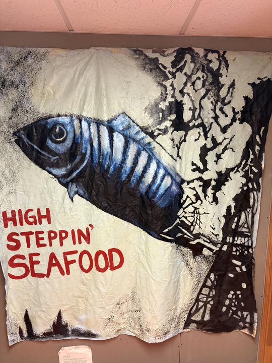 Hand-painted High Steppin' Seafood stage banner: a large blue fish flying over a burning black tower
